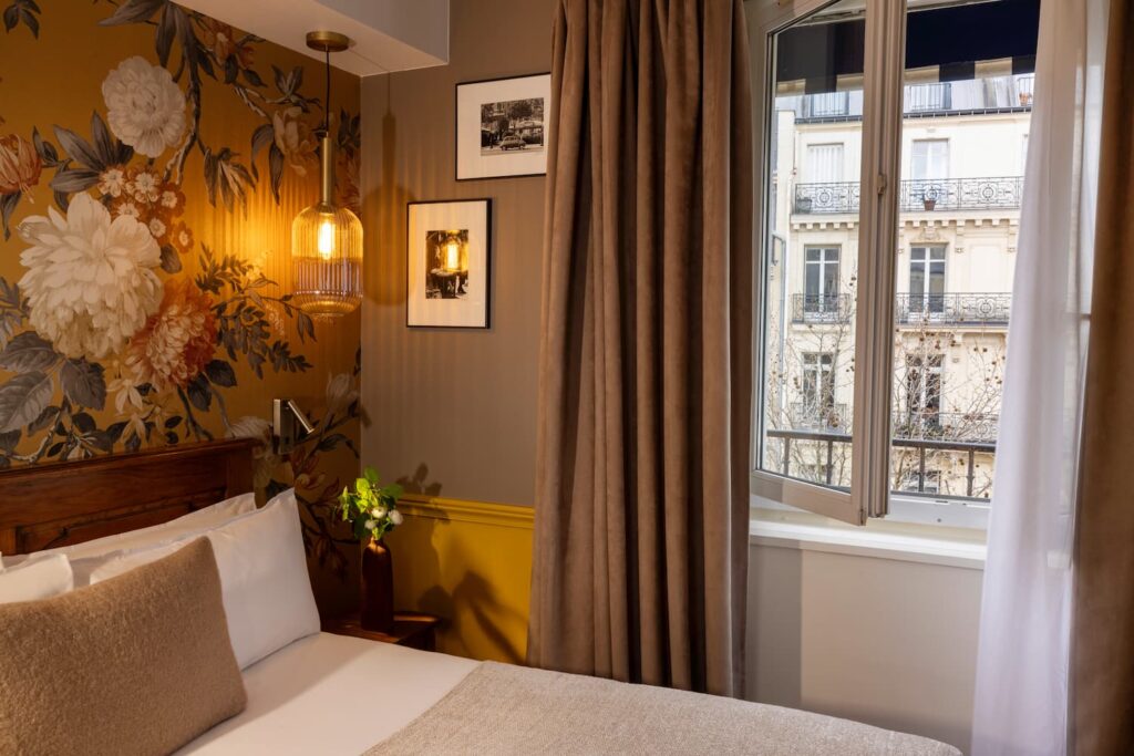 chambre avec lit, papier peint, rideau et vue sur paris - Welcome Hôtel rue de seine paris